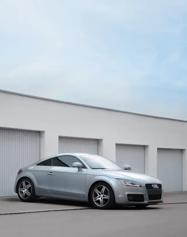 Coupé sportif gris argent garé devant une rangée de box de garage blancs.