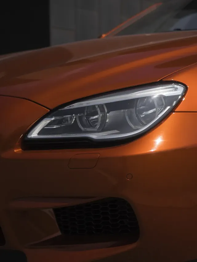 Gros plan sur le phare avant d’un coupé orange, feux allumés.