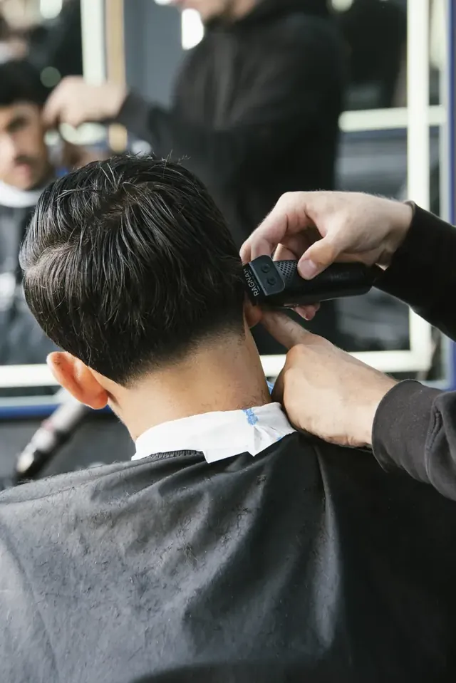 Coupe en cours, tondeuse sur la nuque d’un client vu de dos.