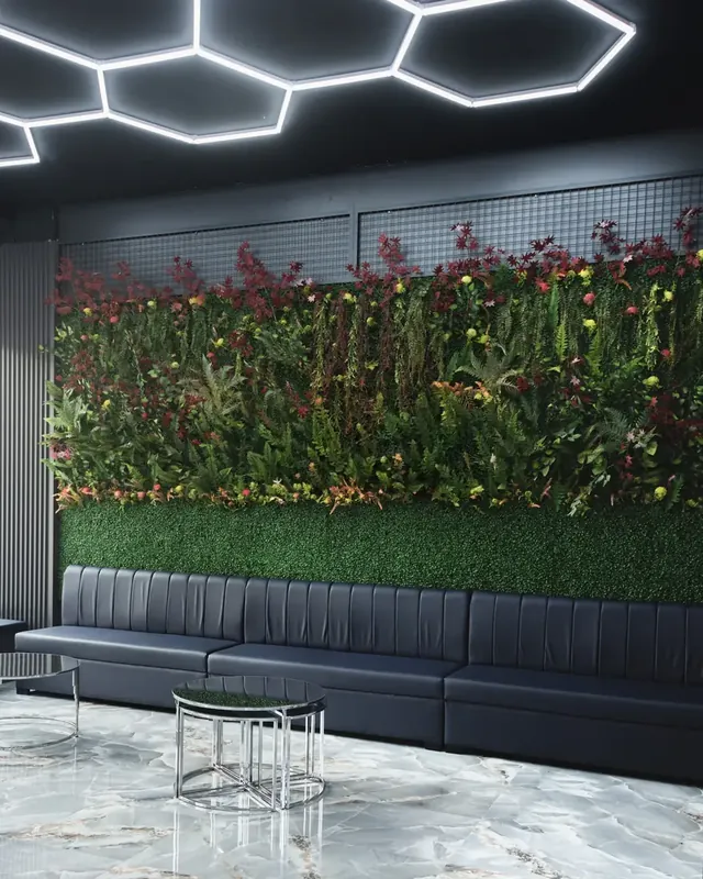 Salle d’attente d’un barbershop : banquette noire, mur végétal et plafonniers hexagonaux.