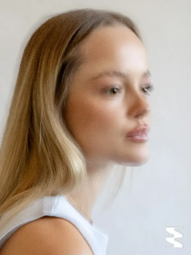 Portrait de profil d’une femme blonde sur fond clair.
