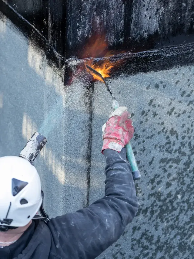 Ouvrier en casque chauffant au chalumeau un relevé d’étanchéité en toiture.