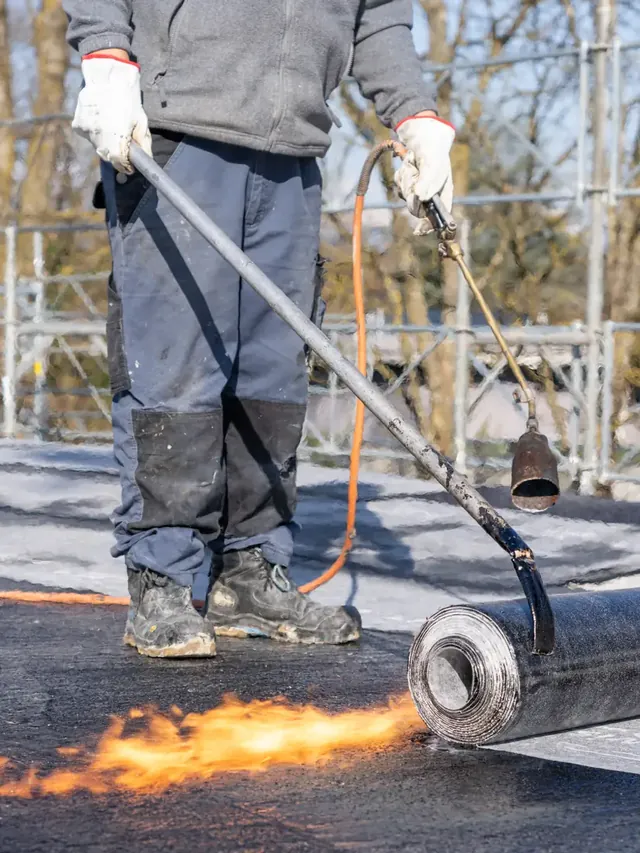 Pose d’un rouleau d’étanchéité au chalumeau sur une toiture plate.