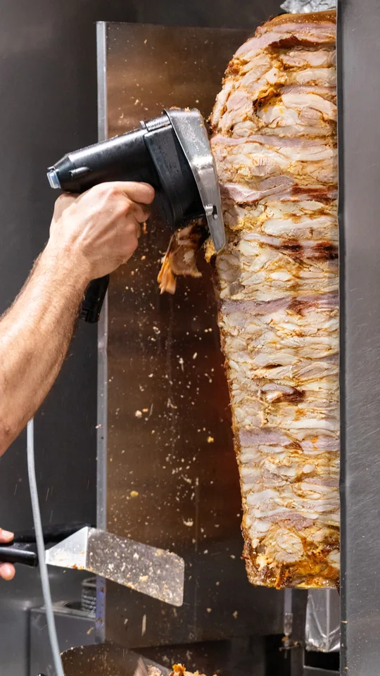 Broche de kebab dans la cuisine du restaurant, la viande tranchée à la lame électrique.