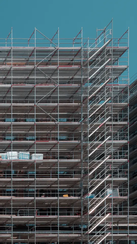 Façade d’un immeuble en construction, entièrement couverte d’échafaudages, sur ciel bleu.