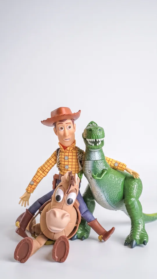 Figurines de collection posées sur fond blanc : un cow-boy, son cheval et un dinosaure vert.